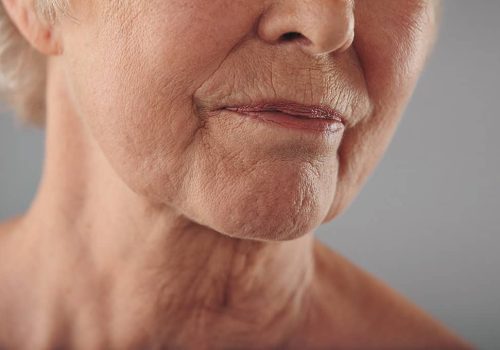 Macro of a senior female face with wrinkled skin against grey background. Cropped old woman face.
